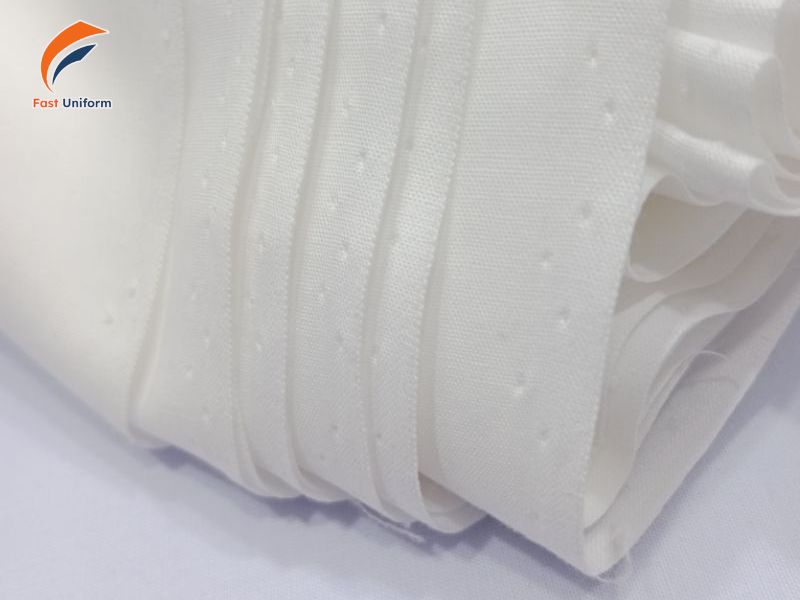 Áo đồng phục trắng nên may bằng cotton, linen, vải dệt pha, satin hoặc blend bền đẹp, giữ phom tốt